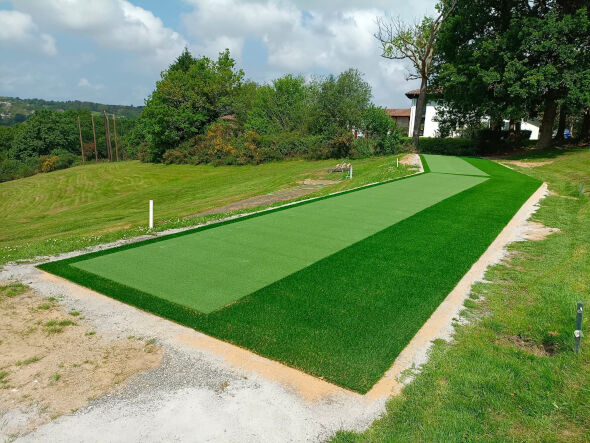 Greenwich Outdoor tee line consisting of one continuous green synthetic grass strip surrounded by trees